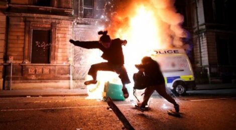 a skateboarder does a trick in front of a burning police van in Bristol