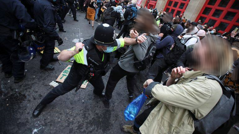 A police officer outside bridewell pushes a protester whilst getting ready to hit them with a baton, the crowd is passive. 