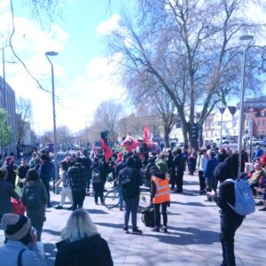 a crowd with red and black flags gathering around the empty Colston plinth