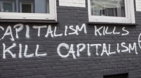 a building with spray paint on the side reading 'Capitalism Kills, Kill Capitalism' with a circle A