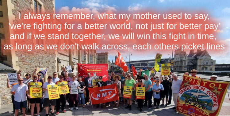 dozens of RMT union members outside Temple Meads train station, they have flags and banners. Above them on the text has been added "i always remember what my mother used to say ,we're fighting for a better world not just for better pay, and if we stand together we will win this fight in time, as long as don't walk across each others picket lines
