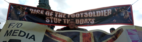 A fascist demonstrater lears down from between two banners one reads 'rise of the footsoldiers, stop the boats'